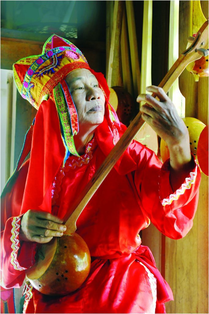 Then shaman in red ceremonial costume playing a dan tinh lute indoors