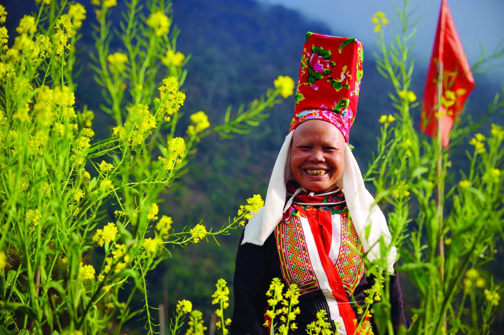 Người phụ nữ dân tộc mặc trang phục truyền thống giữa ruộng hoa cải vàng