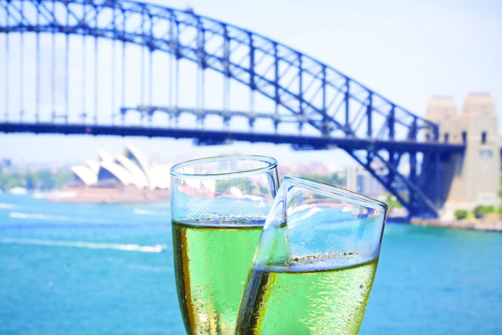 Hai ly rượu sủi tăm đặt trước Cầu cảng Sydney và Nhà hát Opera Sydney mờ ảo