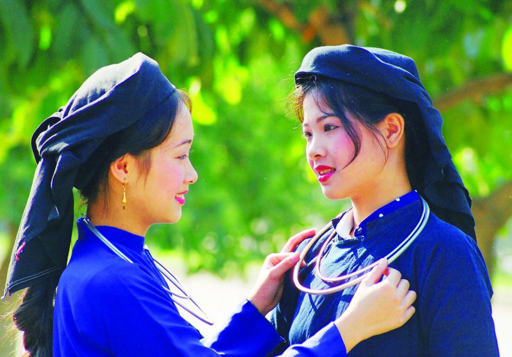 Two women in traditional Tay clothing adjusting silver neck rings