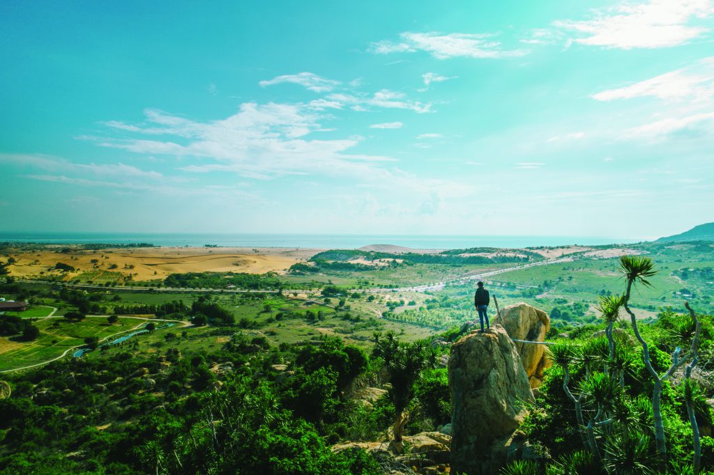 Traveler standing on a rocky viewpoint overlooking coastline and dunes