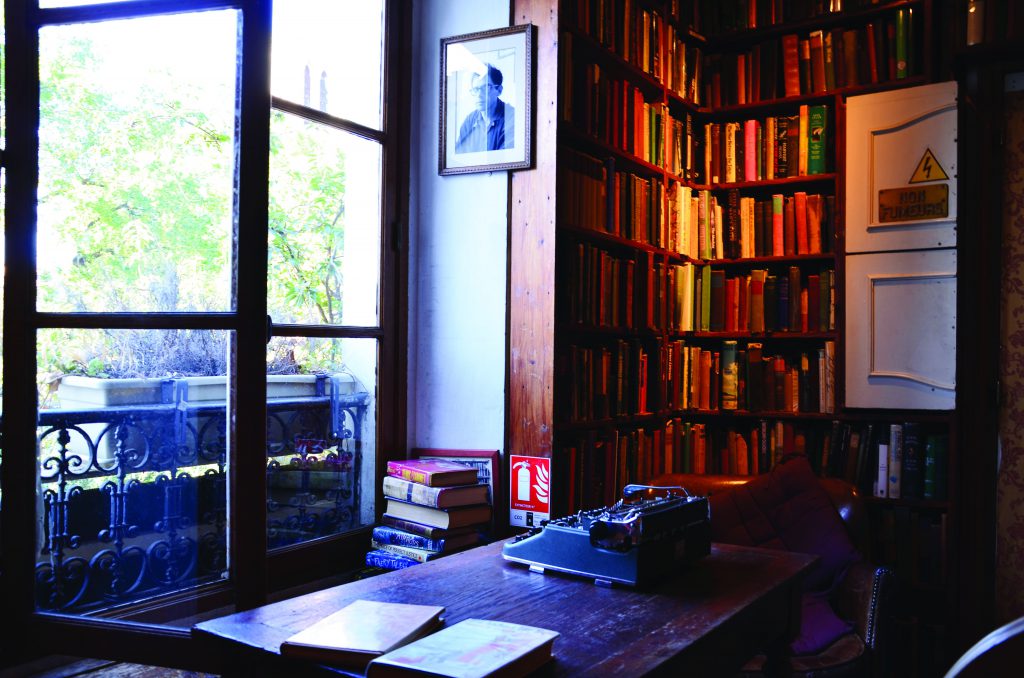 Bàn gỗ với máy đánh chữ bên cửa sổ, kệ sách cũ ở Shakespeare and Company