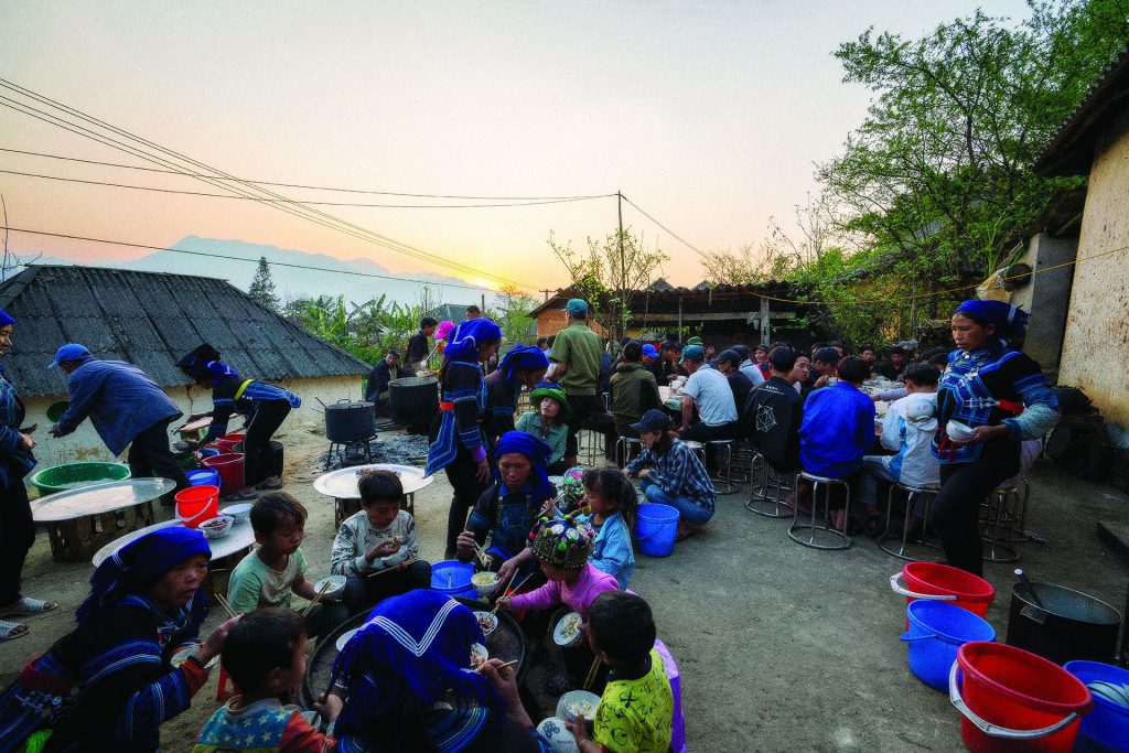 Village courtyard feast at sunset with Ha Nhi families sharing a communal meal outdoors
