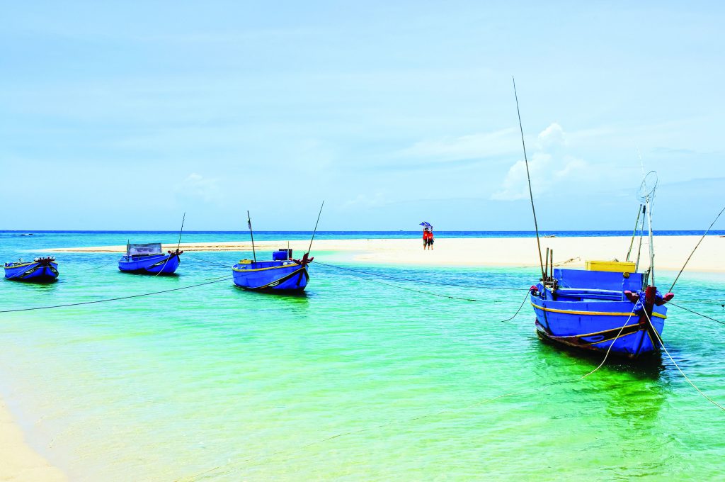 Blue fishing boats anchored in shallow turquoise water near a sandbar