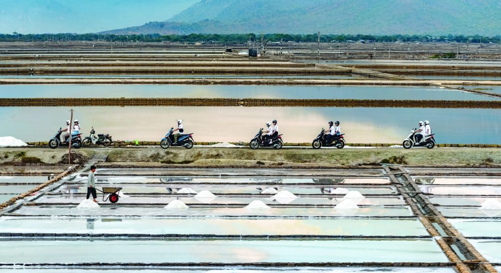 Đoàn xe máy chạy qua cánh đồng muối với những ô nước phản chiếu dưới chân núi