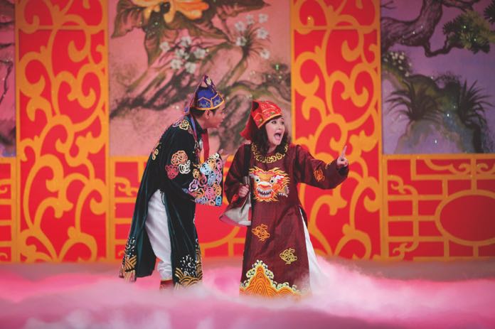 Performers in elaborate imperial-style costumes participating in a Tao Quan theatrical performance with a foggy stage floor.