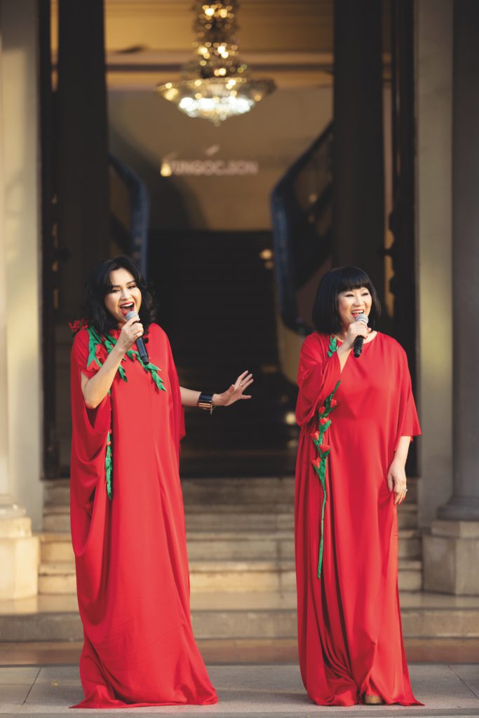 Người mẫu trong chiếc váy xanh lá cây đính hoa hồng dọc thân váy đứng trước thềm nhà cổ.