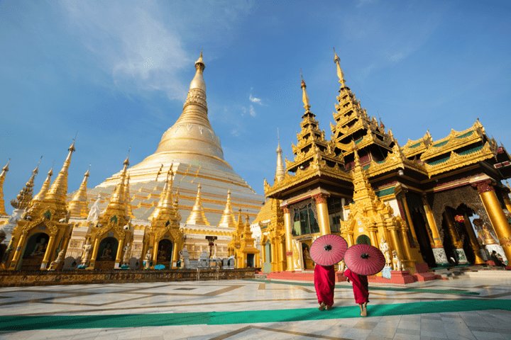 Two monks walk past a stunning golden temple complex under a bright blue sky