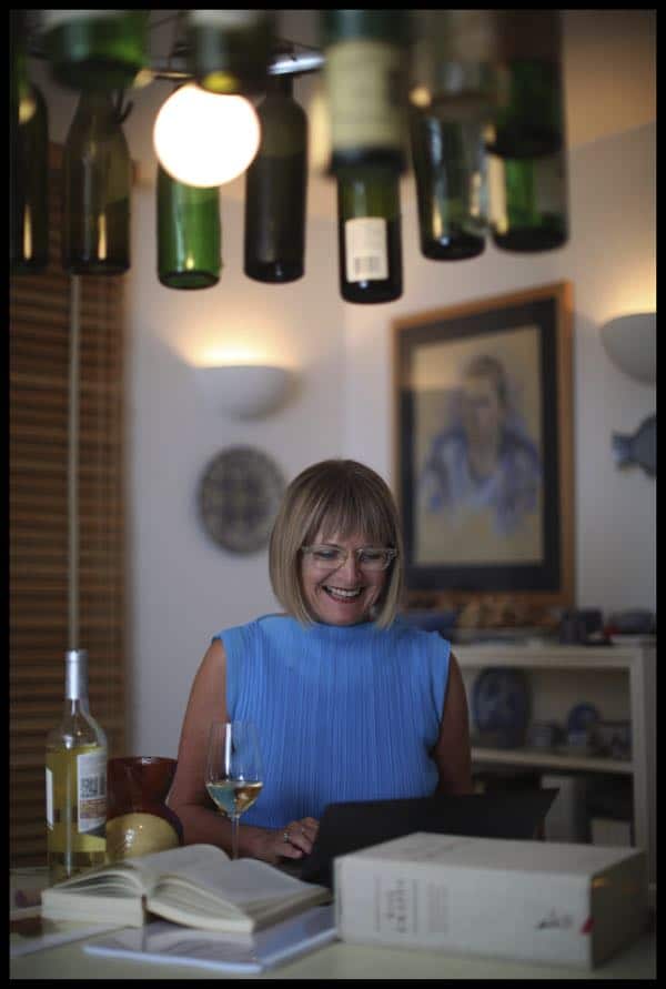 Nữ chuyên gia rượu vang Jancis Robinson mỉm cười rạng rỡ khi đang làm việc bên ly rượu và những cuốn sách.