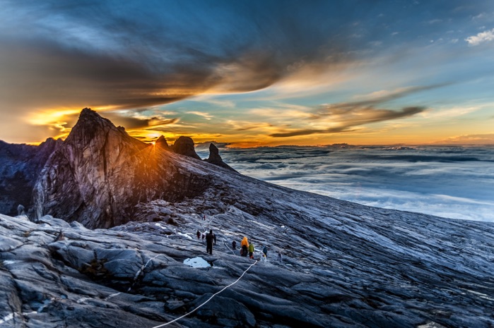 Các nhà leo núi đang chinh phục đỉnh Kinabalu hùng vĩ giữa biển mây bồng bềnh lúc hoàng hôn.