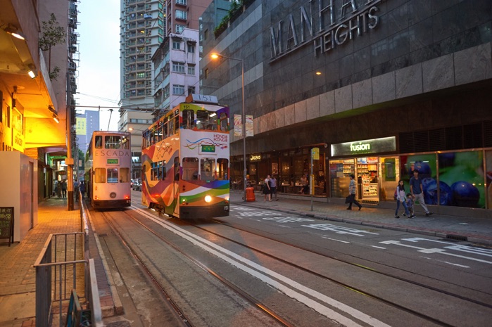 Hong Kong trams travel along city streets lined with tall buildings and shops