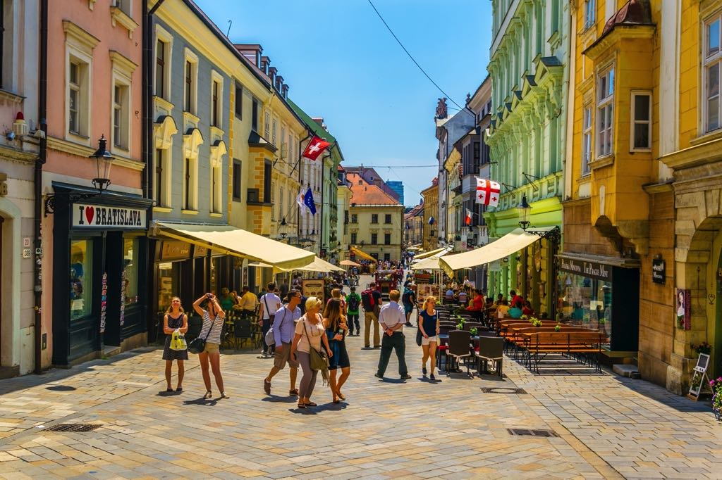 Khách du lịch đi dạo trên con phố đi bộ sầm uất với các nhà hàng ngoài trời ở Bratislava