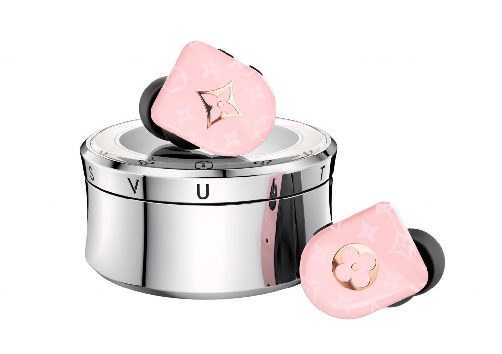 Tai nghe không dây in-ear Louis Vuitton màu hồng nhạt nữ tính đặt cạnh hộp sạc kim loại sáng bóng