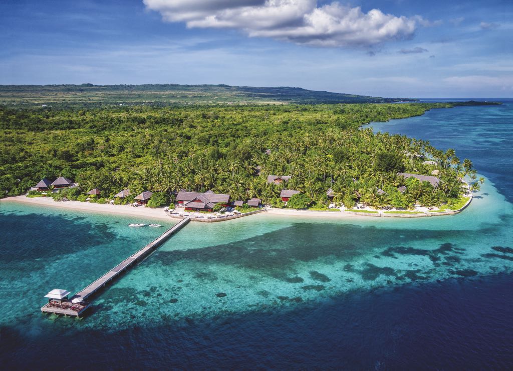 Lush tropical island features beachside bungalows and a long wooden pier