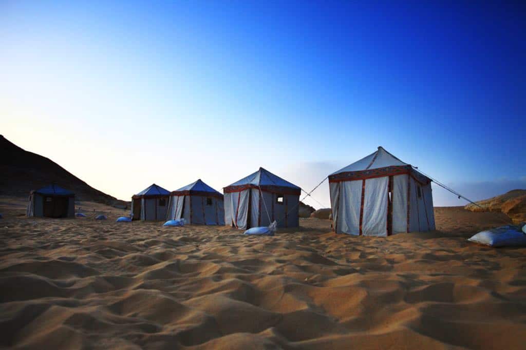 Desert tents sit on golden sand under a clear blue sky