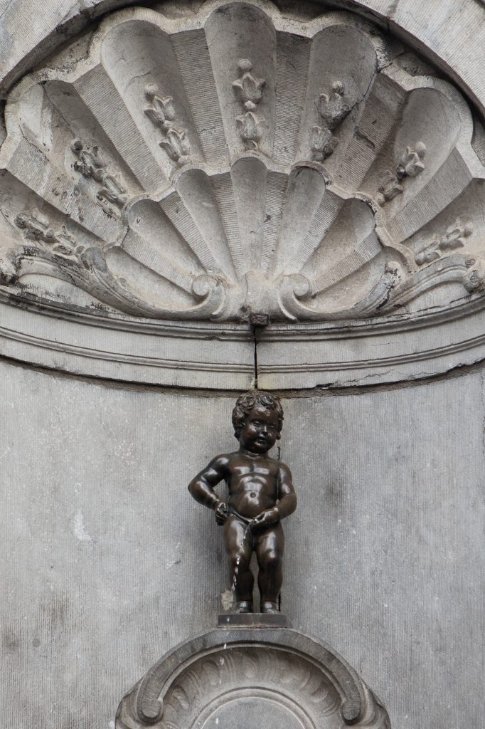 A bronze statue of a small boy urinates into a basin below ornate stonework