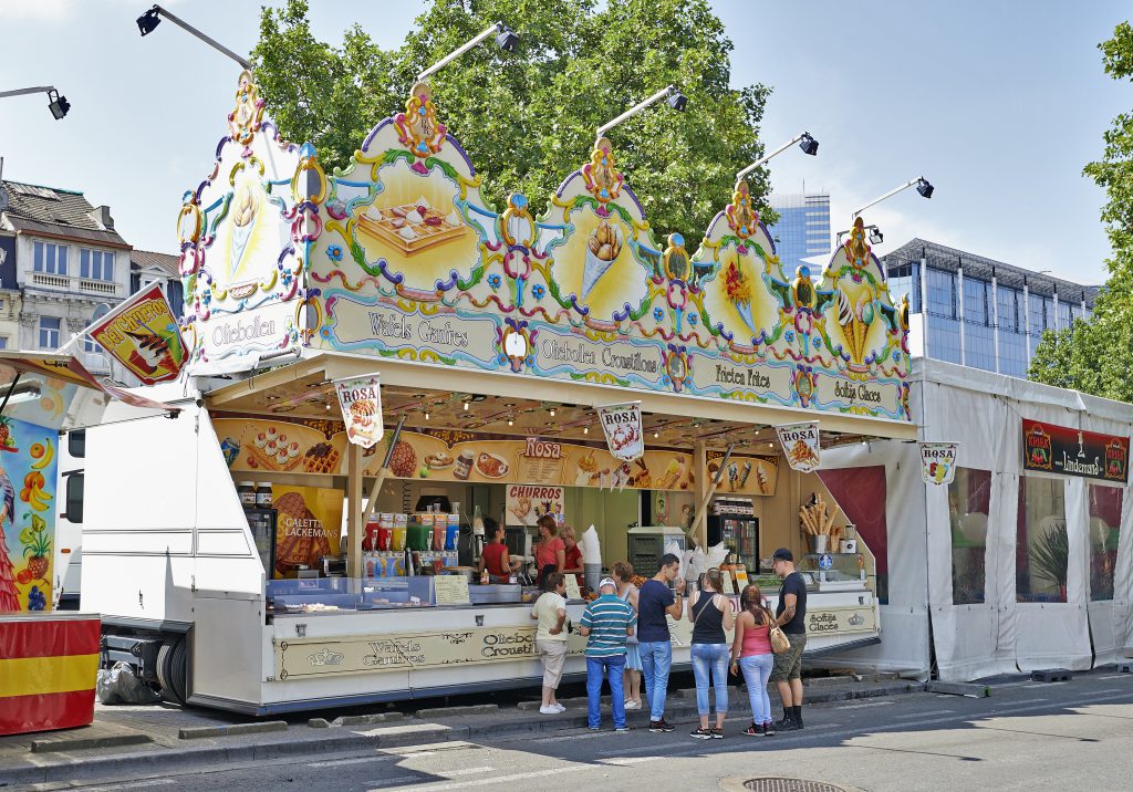 People line up at a brightly decorated food stand selling waffles and churros