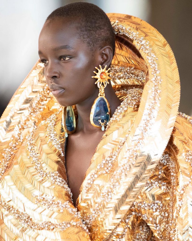 Người mẫu da màu với trang phục haute couture màu vàng kim lấp lánh và hoa tai lớn
