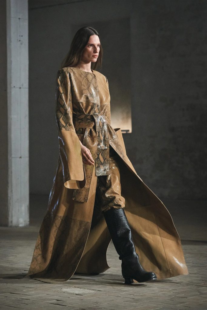 Người mẫu trình diễn áo khoác dài và ủng đen trên sàn diễn thời trang