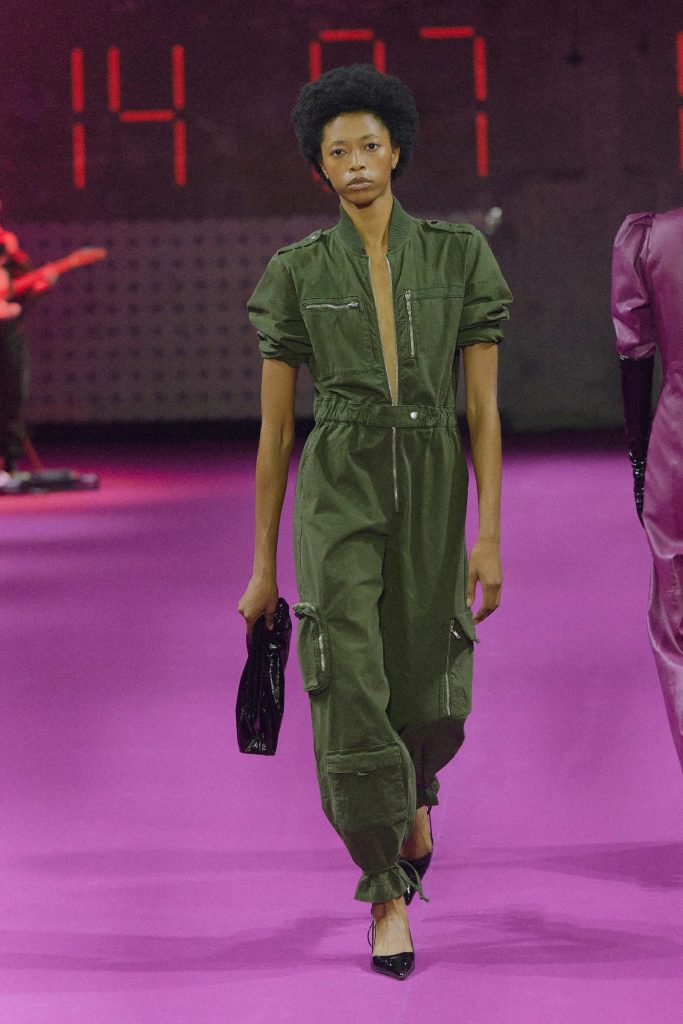 Người mẫu trình diễn bộ jumpsuit xanh rêu trên sàn diễn thời trang màu tím