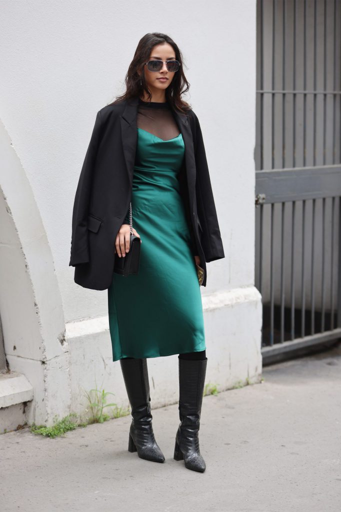 Cô gái mặc váy lụa xanh lá cây kết hợp áo khoác đen và ủng cao gót trên phố