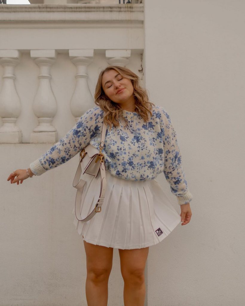 Cô gái mặc áo hoa và váy trắng tạo dáng bên bức tường trắng