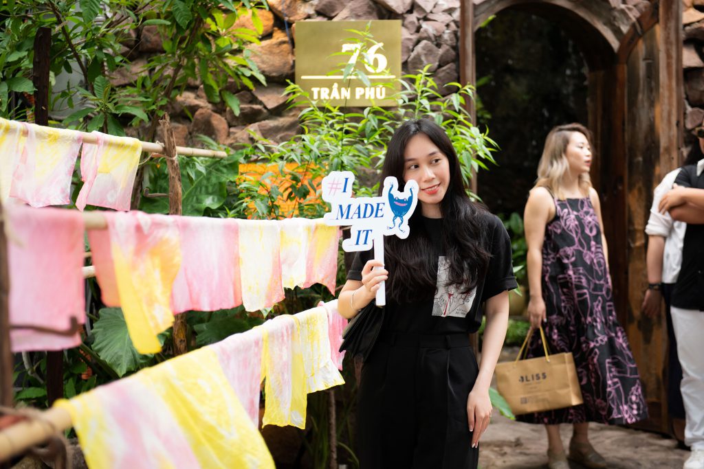 Cô gái trẻ cười rạng rỡ bên những dải vải màu pastel và biển hiệu "I MADE IT"