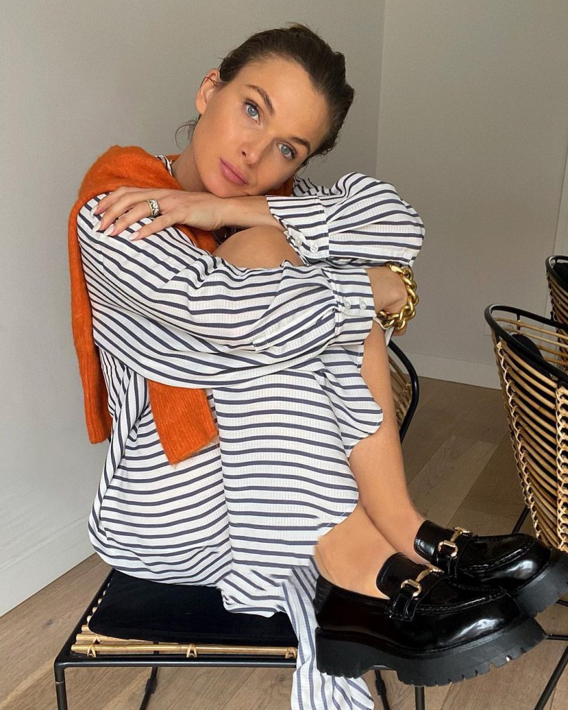 Cô gái trẻ diện váy sọc ngang và áo len cam tựa vào ghế đen