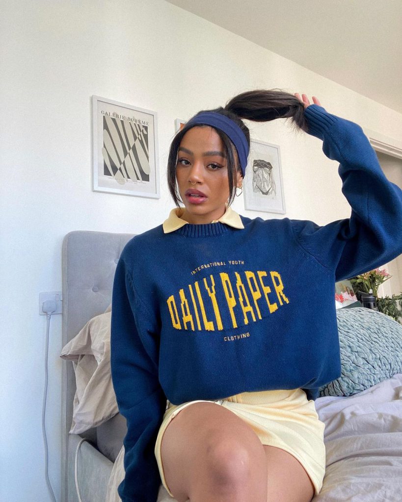 Cô gái mặc áo len xanh đậm và váy xếp ly màu be tạo dáng trong phòng