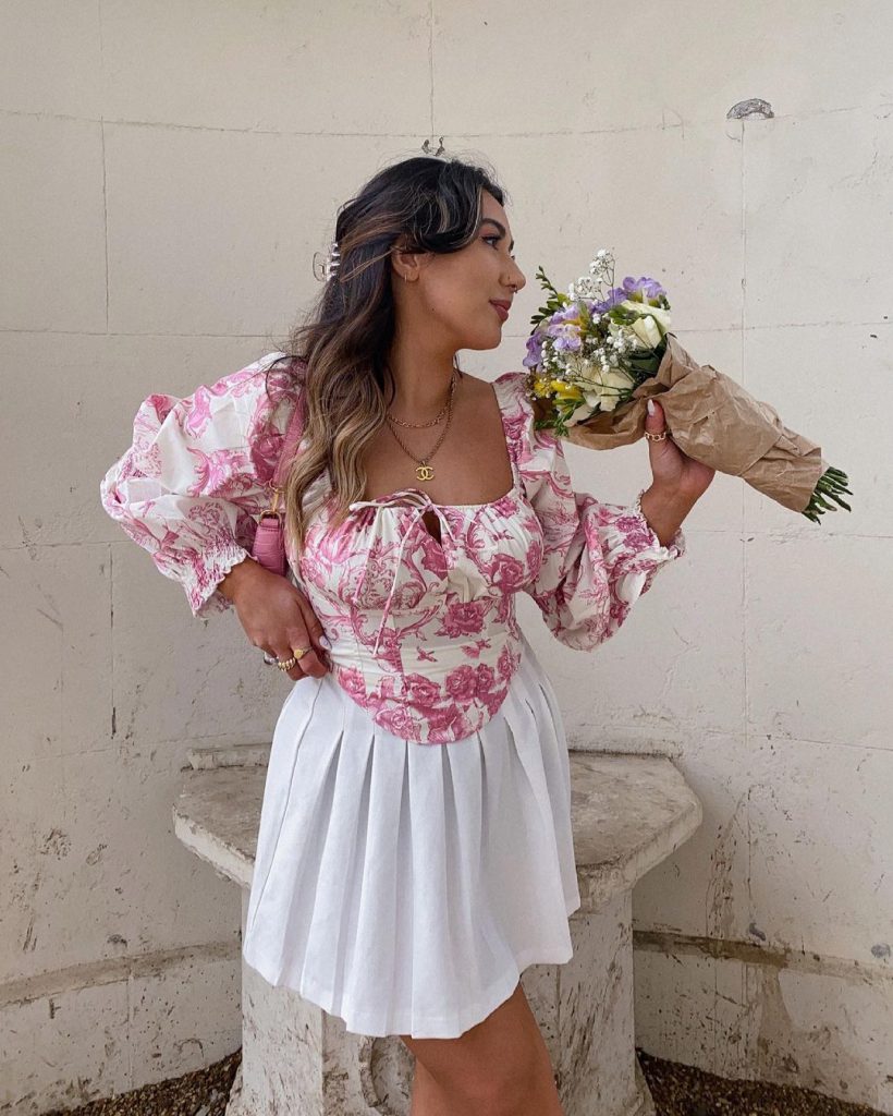 Cô gái trẻ diện váy hoa tay bồng cầm bó hoa tươi tắn tạo dáng bên tường trắng