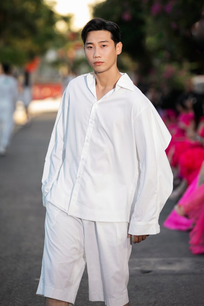 Người mẫu mặc trang phục trắng rộng rãi sải bước trên sàn diễn ngoài trời