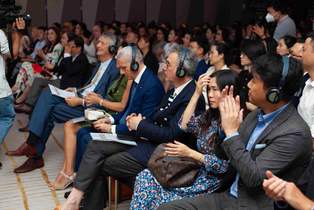 Khán giả lắng nghe và vỗ tay tại một sự kiện thời trang với nhiều người đeo tai nghe
