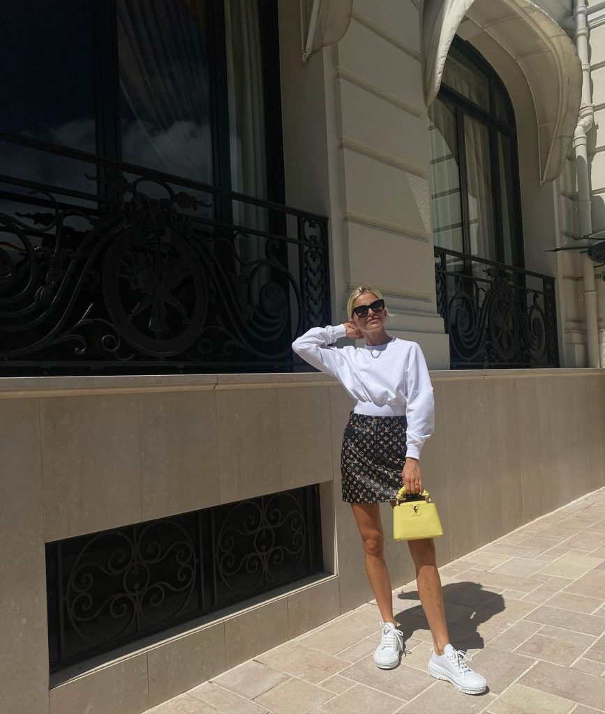 Cô gái mặc áo trắng và váy ngắn họa tiết đeo túi xách màu vàng đứng tạo dáng trên phố