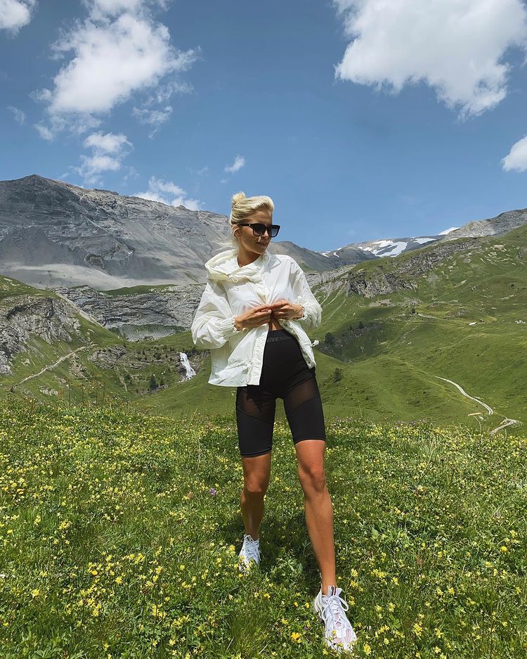 Cô gái mặc đồ thể thao đi bộ trên đồng cỏ xanh mướt có núi ở phía xa