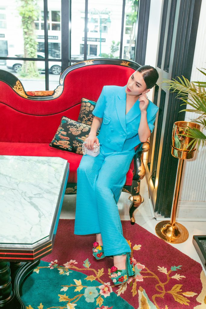 Cô gái mặc bộ vest xanh ngồi trên ghế sofa đỏ trong phòng khách sang trọng