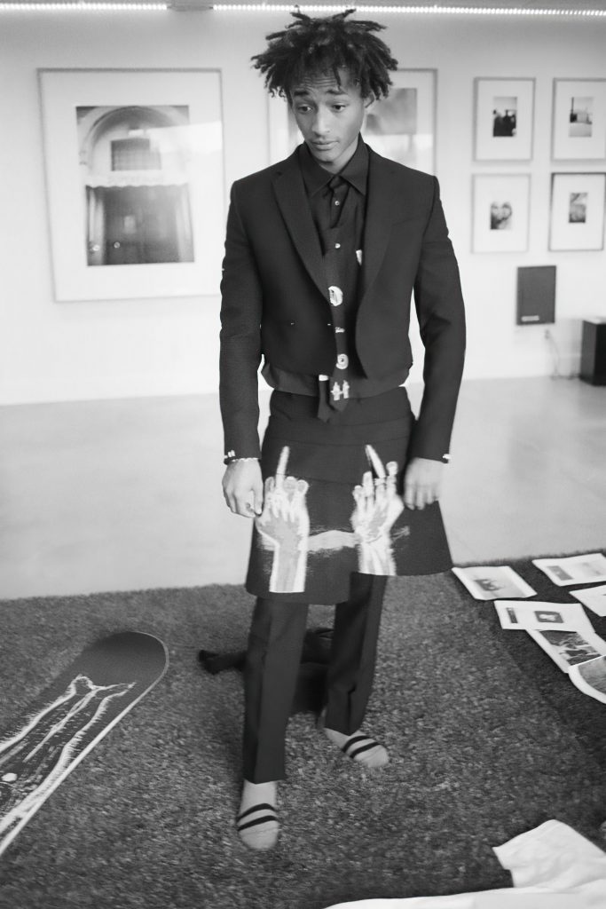 Người đàn ông mặc vest đen và váy in hình tay đang tạo dáng trong phòng trưng bày nghệ thuật