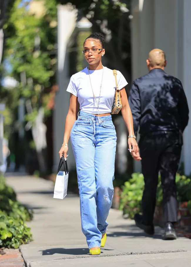 Cô gái mặc áo trắng và quần jean đi trên vỉa hè nắng sáng