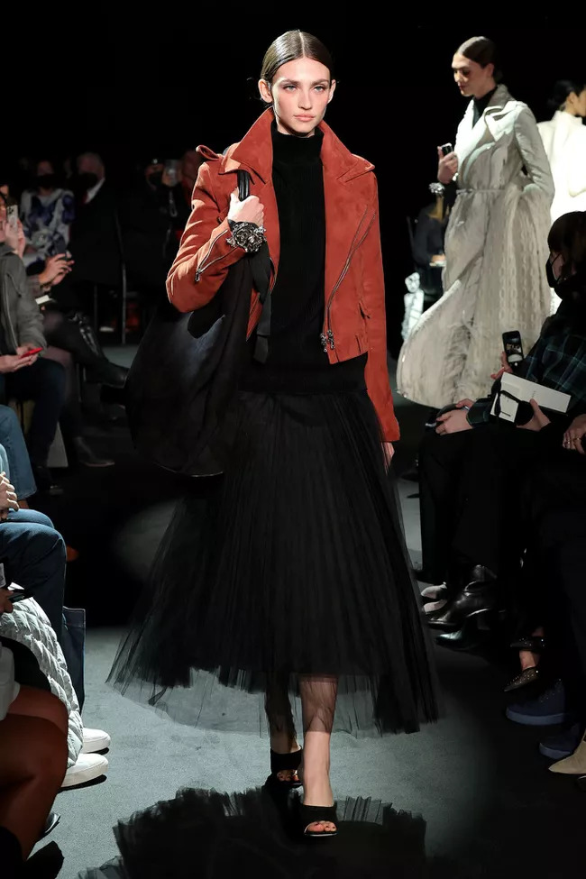 Người mẫu trình diễn chân váy tulle đen kết hợp áo len và áo khoác da cam trong buổi trình diễn thời trang