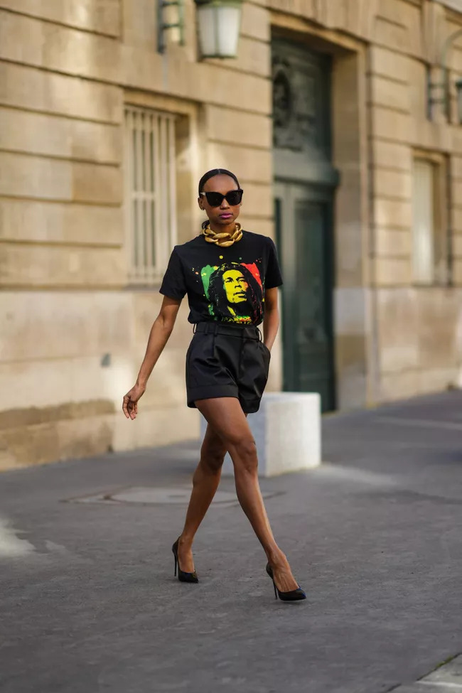 Người mẫu da màu diện áo phông in hình và quần short đen đang bước đi trên phố