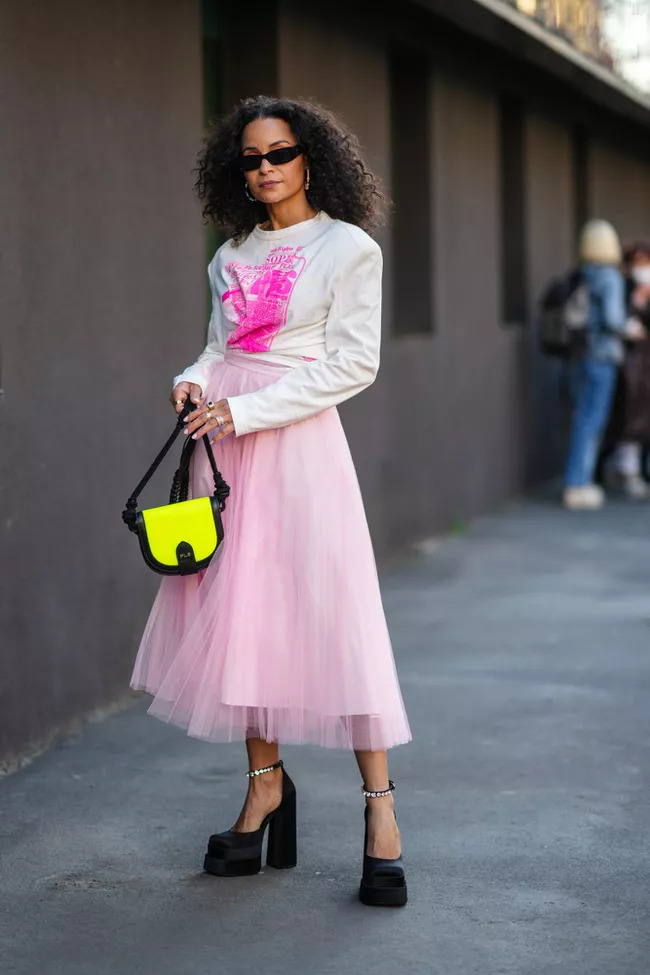 Cô gái mặc áo trắng và chân váy tulle hồng pastel đi giày cao gót đen