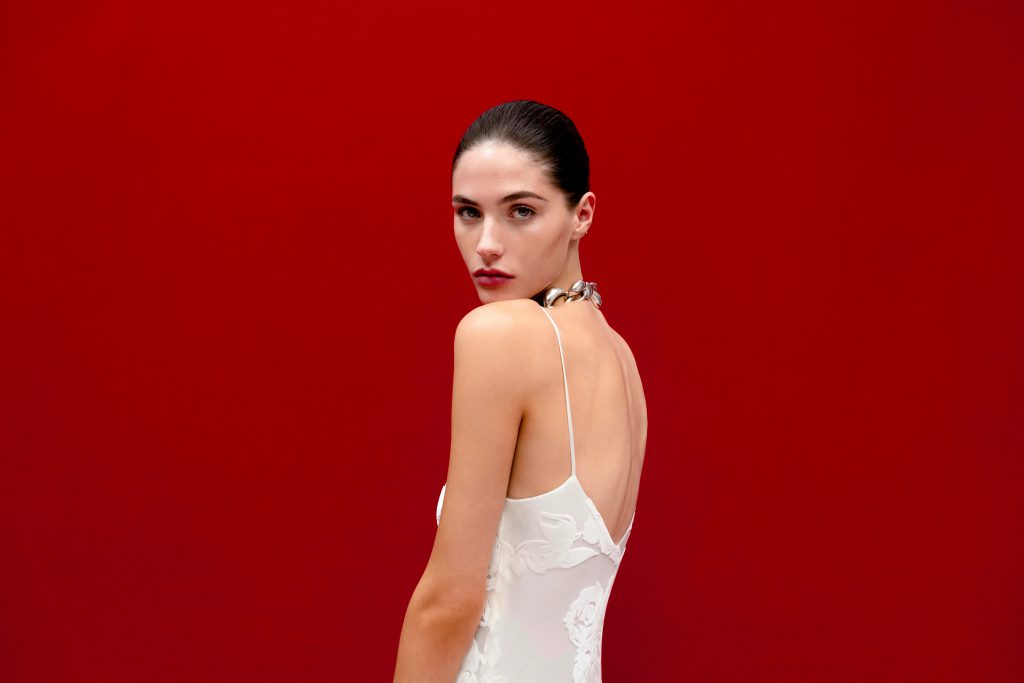 Người mẫu mặc váy trắng tinh tế nhìn về phía người xem trên nền đỏ rực