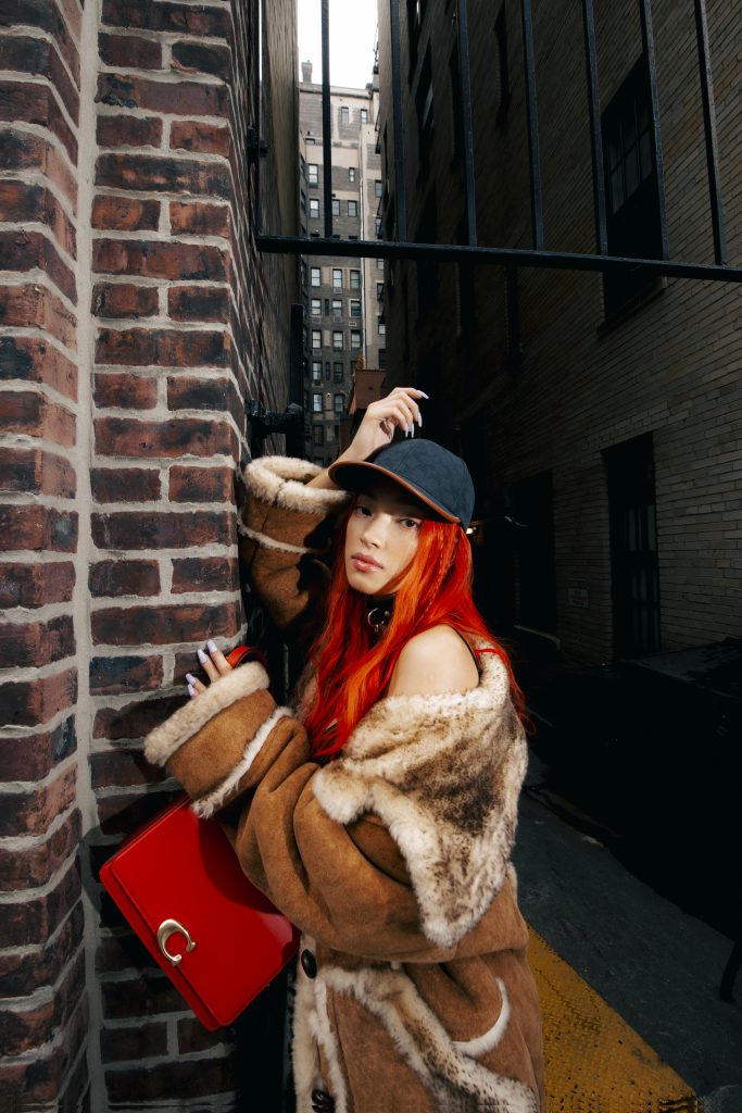 Người mẫu tóc đỏ đội mũ lưỡi trai và khoác áo lông đang tạo dáng giữa phố