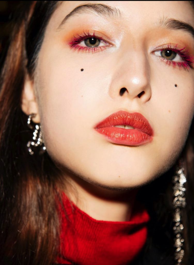 Chân dung cô gái trang điểm mắt và môi màu đỏ nổi bật với nốt ruồi trên má