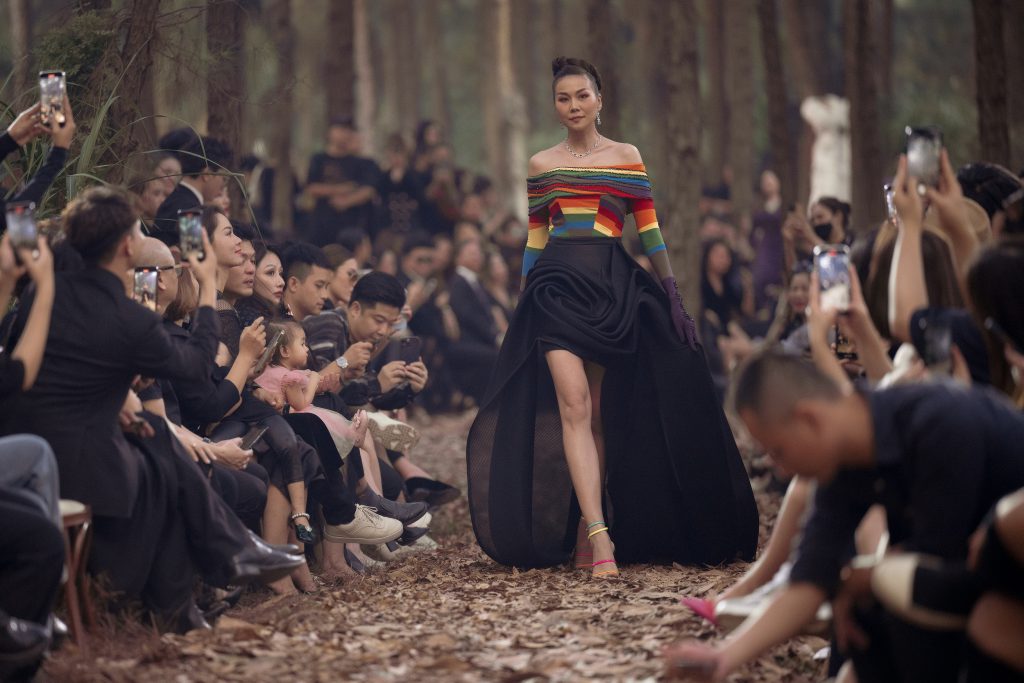 Người mẫu sải bước trên sàn diễn ngoài trời giữa rừng cây với trang phục nổi bật