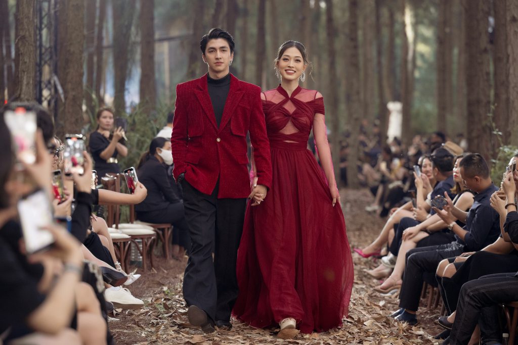 Người mẫu nam và nữ diện trang phục đỏ nổi bật sải bước trên sàn diễn ngoài trời