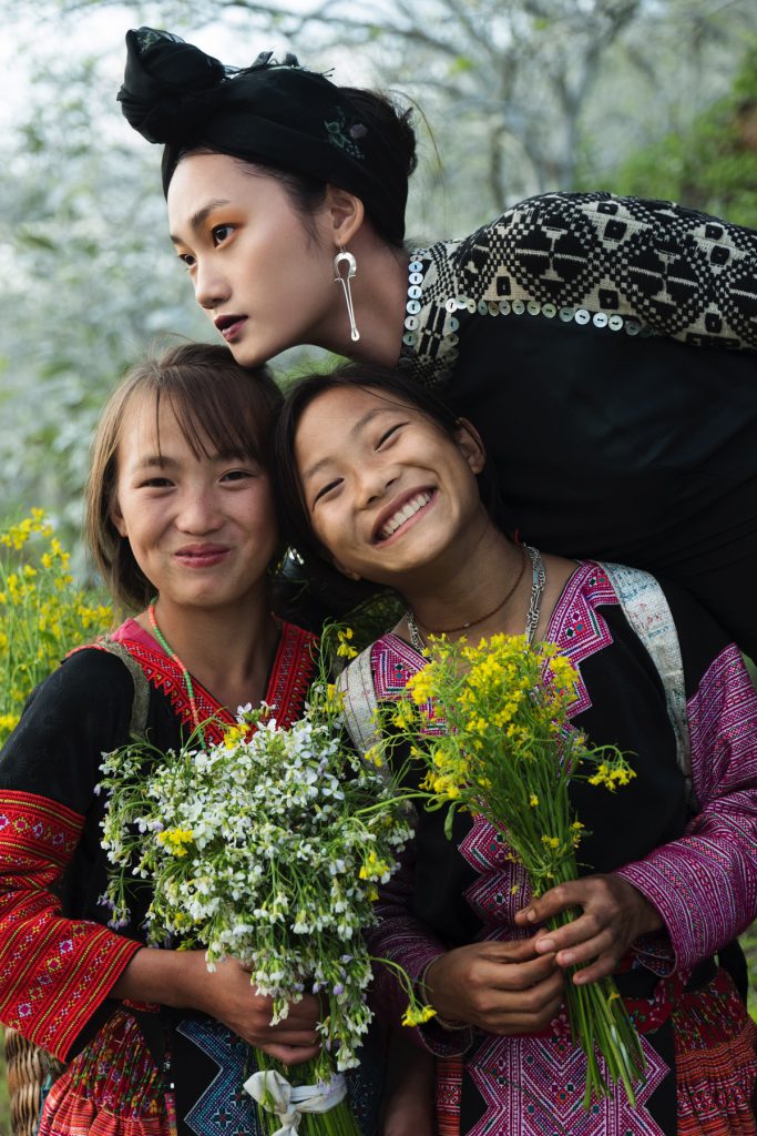 Ba thiếu nữ mặc trang phục dân tộc ôm nhau giữa đồng hoa vàng tươi