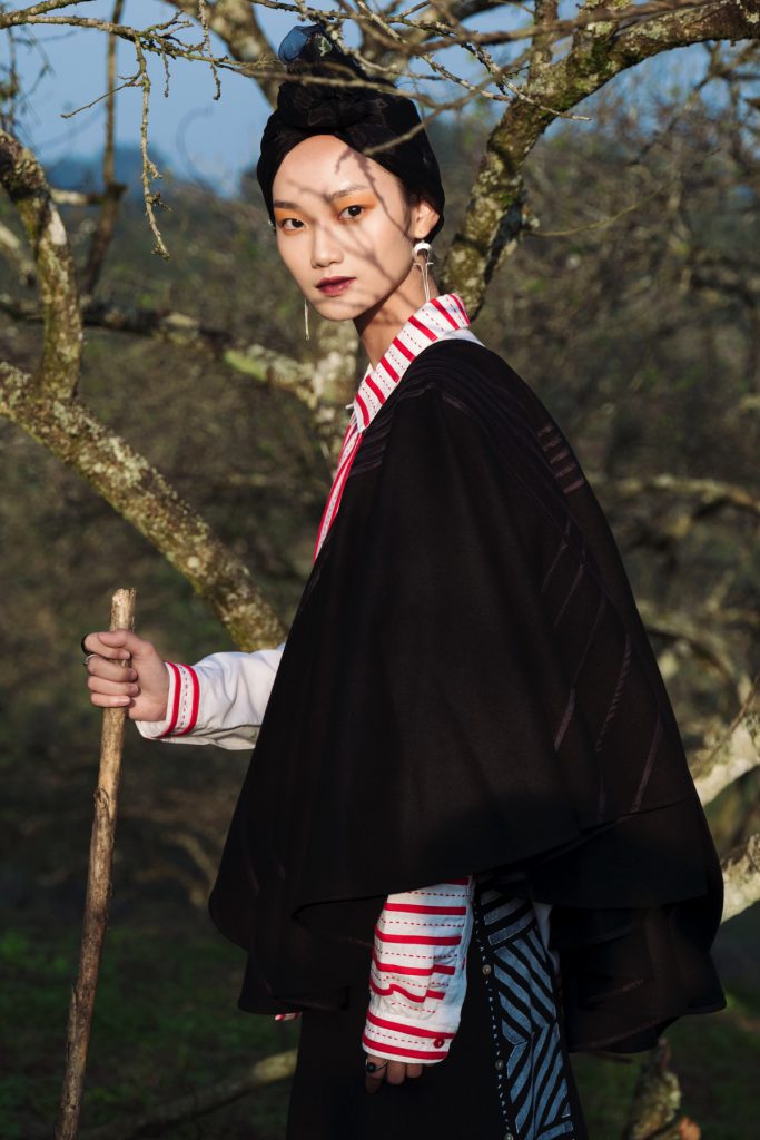 Người đàn ông mặc trang phục dân tộc H’Mông truyền thống đứng dưới gốc cây