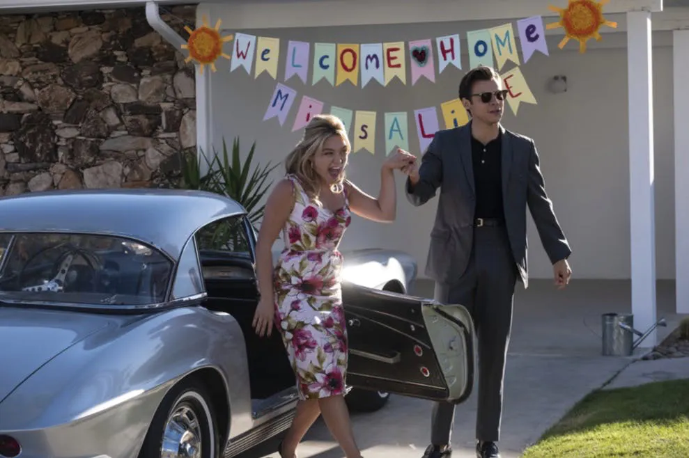 Cặp đôi trẻ trung bước ra từ xe hơi cổ điển với dòng chữ chào mừng được treo phía sau