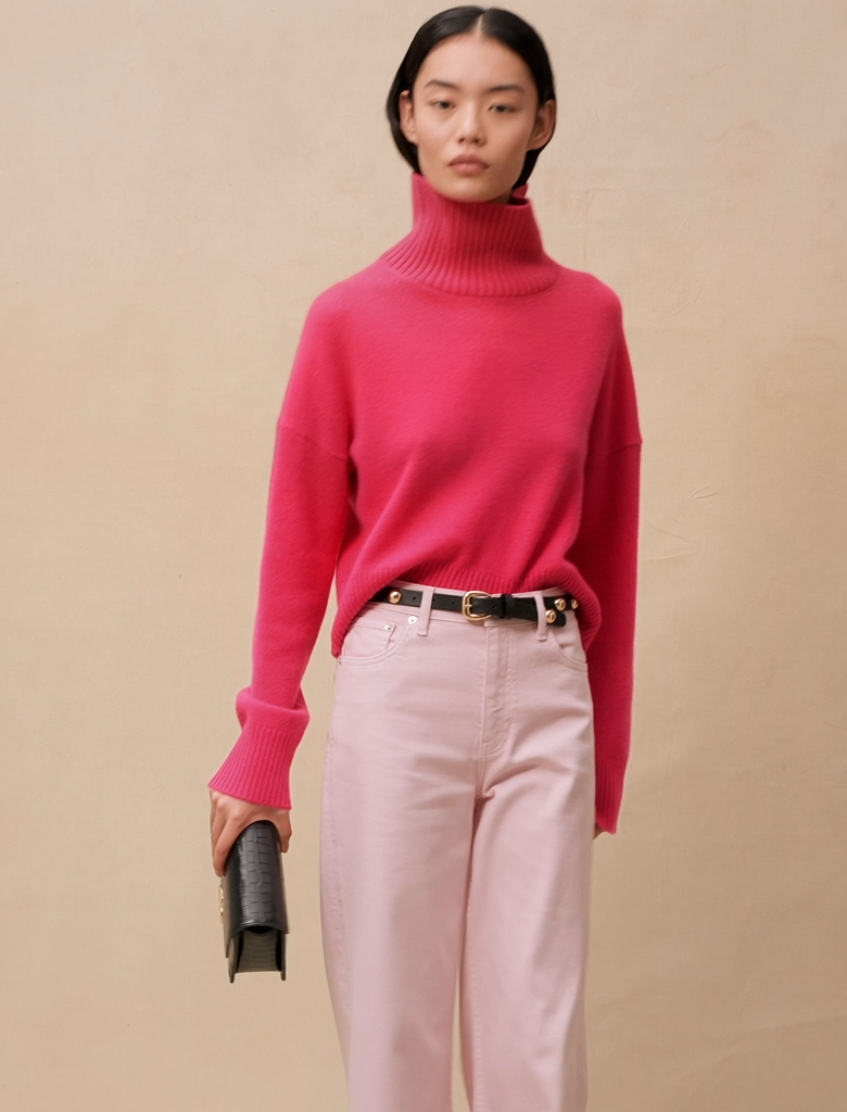 Người mẫu mặc áo len hồng và quần màu hồng nhạt cầm túi xách đen