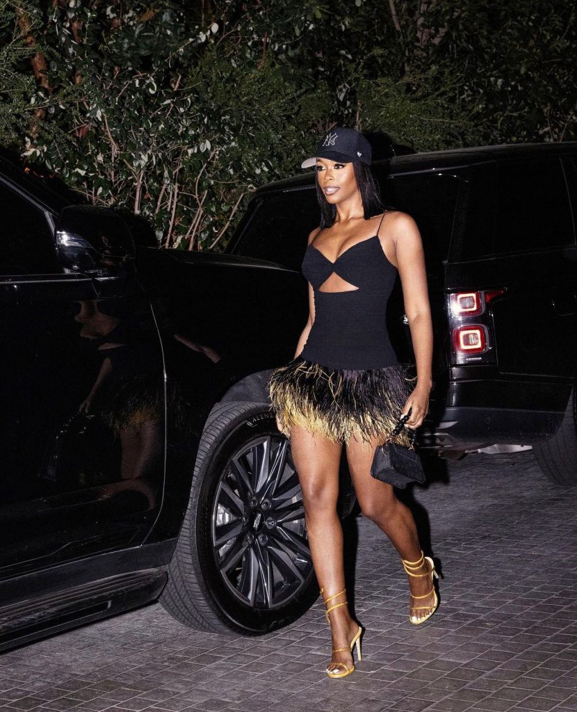 Nữ ca sĩ mặc váy đen xẻ tà và đội mũ lưỡi trai đang bước xuống xe hơi sang trọng